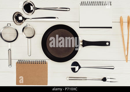 Vista dall'alto dei libri di testo, padella e utensili da cucina in legno bianco tabella Foto Stock