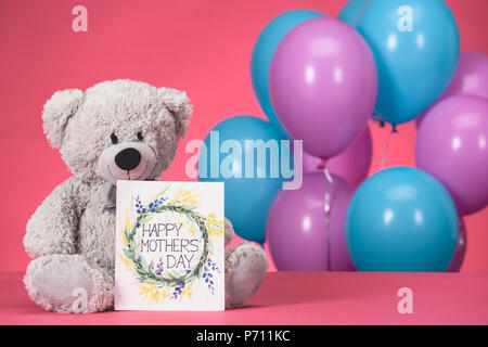 Orsacchiotto di peluche e una cartolina con testo Felice Festa della Mamma Rosa sul piano portapaziente Foto Stock
