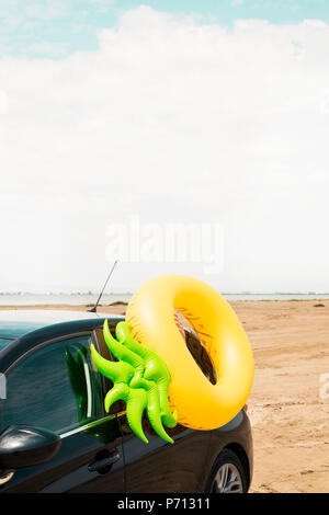 Un anello di nuotare in forma di ananas su una vettura, sulla sabbia di una spiaggia, con il mare in background, con qualche spazio vuoto sulla parte superiore Foto Stock