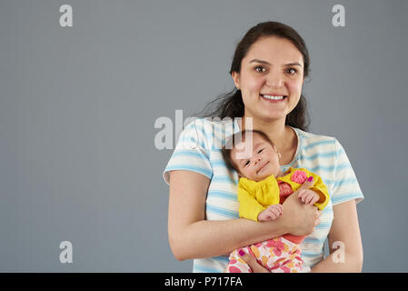 Giovane madre ispanica con piccolo grazioso Baby girl isolato su sfondo grigio ritratto Foto Stock