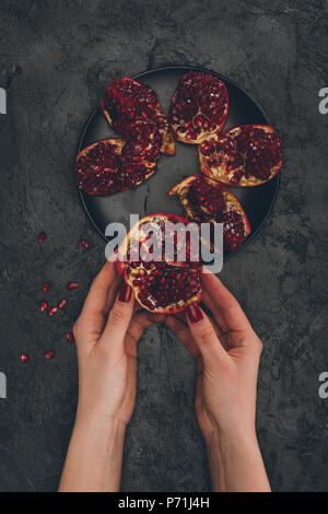 Immagine ritagliata della donna prendendo spicchio di melagrana dalla piastra nera Foto Stock