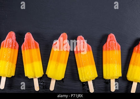 Lime e orange gelati su stick su nero ardesia bordo. Focus su Popsicles. Foto Stock