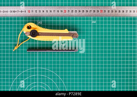 Taglierina, ruller e matita su un verde tappeto di taglio in background Foto Stock