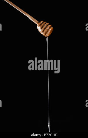 Il miele che gocciola dalla miele in legno stick isolato su nero Foto Stock