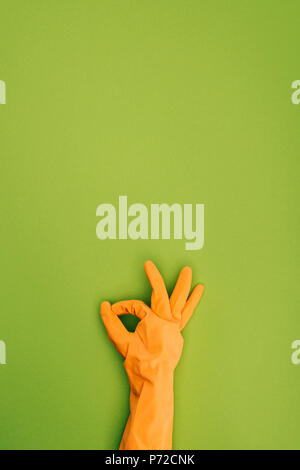 Immagine ritagliata della donna che mostra ok sign in gomma protettivo guanto isolato su verde Foto Stock