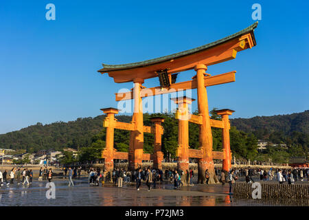 I turisti a piedi sotto la porta torii di Miyajima a bassa marea, Itsukushima, sito Patrimonio Mondiale dell'UNESCO, Prefettura di Hiroshima, Honshu, Giappone, Asia Foto Stock