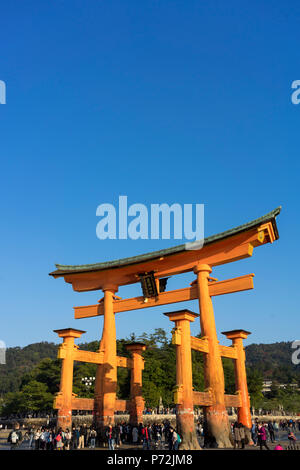 I turisti a piedi sotto la porta torii di Miyajima a bassa marea, Itsukushima, sito Patrimonio Mondiale dell'UNESCO, Prefettura di Hiroshima, Honshu, Giappone, Asia Foto Stock