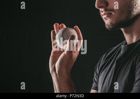 Ritagliato shot del giovane sportivo barbuto tenendo palla da baseball isolato su nero Foto Stock