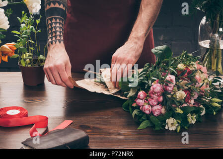 Immagine ritagliata del fioraio maschio con tatuaggio sul lato bouquet di incarto nella confezione di carta Foto Stock