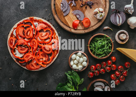 Vista superiore della pizza cruda con ingredienti diversi su cemento tabella Foto Stock