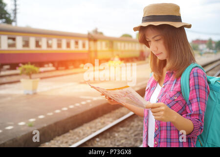 Giovane donna viaggiatore con zaino e hat presso la stazione dei treni e alla ricerca sulla mappa per piano di viaggio, concetto di viaggio Foto Stock