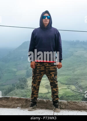 Escursionista uomo ritratto di trekking in alta montagna. Escursionismo maschio in alpine abbigliamento hard shell jacket sopra in montagna sopra le nuvole. Ritratto di giovane uomo outdoorsman. Foto Stock