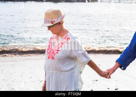 Seguire e vieni con me donna prendere man mano a camminare insieme sulla riva presso la spiaggia. l'oceano in background per amore e il concetto di vacanza Foto Stock