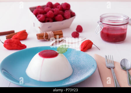 Panna Cotta, dolce tradizionale dolce italiano, con purea di lampone e tocco di red hot Bhut jolokia peperoncino e cannella, decorato con foglie di fre Foto Stock