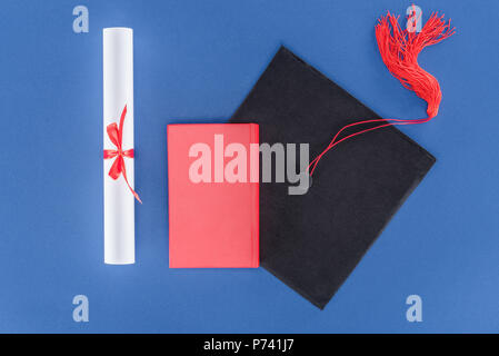 Tappo di graduazione con diploma e prenota isolato su blu Foto Stock