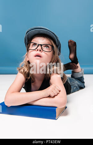 Malinconici capretto piccolo ragazza appoggiata sul libro e guardando in alto Foto Stock