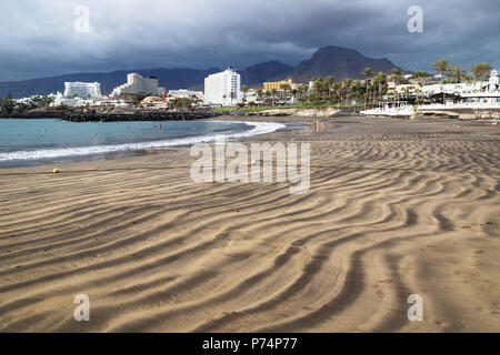 Spiaggia lungo la Costa Adeje con vista su alberghi e le montagne con dark cloudscape, Tenerife, Isole Canarie, Spagna Foto Stock