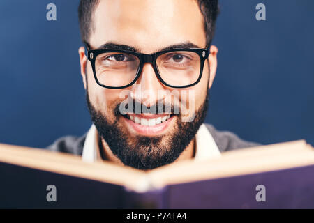 Ritratto di arabo orientale uomo barbuto libro di lettura prima di sfondo blu Foto Stock