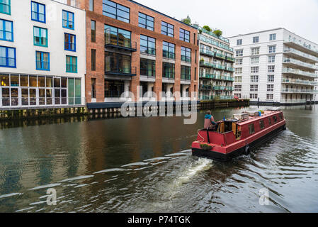 Navigazione della nave al Regent's Canal guidato da un uomo al timone vicino al mercato di Camden con moderni edifici intorno a Londra, Inghilterra, Regno Unito Foto Stock