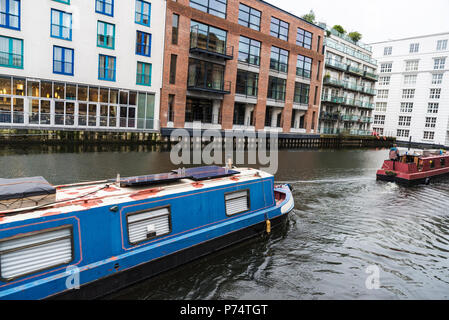 Navigazione della nave al Regent's Canal guidato da un uomo al timone vicino al mercato di Camden con moderni edifici intorno a Londra, Inghilterra, Regno Unito Foto Stock