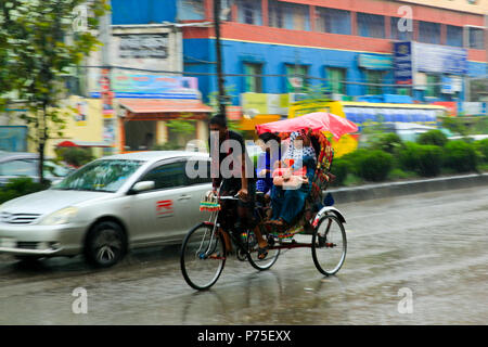 Un rickshaw estrattore porta i suoi passeggeri in giornata piovosa, Dhaka, Bangladesh. Foto Stock