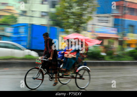 Un rickshaw estrattore porta i suoi passeggeri in giornata piovosa, Dhaka, Bangladesh. Foto Stock