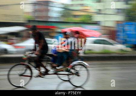 Un rickshaw estrattore porta i suoi passeggeri in giornata piovosa, Dhaka, Bangladesh. Foto Stock