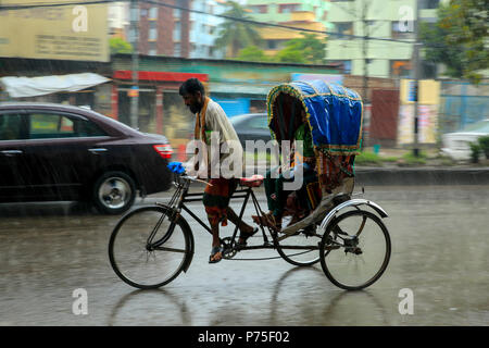 Un rickshaw estrattore porta i suoi passeggeri in giornata piovosa, Dhaka, Bangladesh. Foto Stock