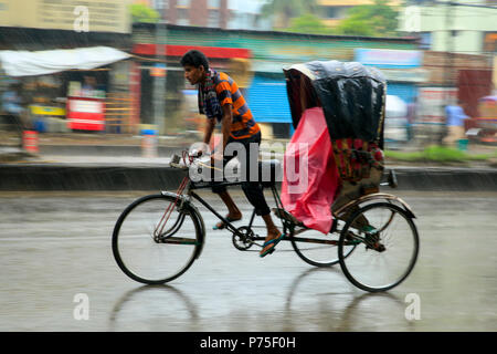 Un rickshaw estrattore porta i suoi passeggeri in giornata piovosa, Dhaka, Bangladesh. Foto Stock