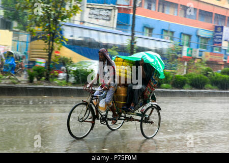 Un rickshaw estrattore porta i suoi passeggeri in giornata piovosa, Dhaka, Bangladesh. Foto Stock