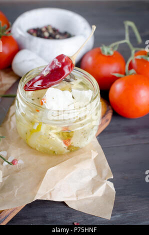 Marinata piccante di feta in un vaso, pomodori da insalata. Su uno sfondo scuro. Copia dello spazio per il tuo testo. Foto Stock