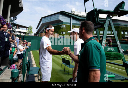 Roger Federer scuote le mani con un membro del personale di terra dopo la pratica su fuori di corte quattro davanti al suo corrispondono più tardi il giorno tre i campionati di Wimbledon al All England Lawn Tennis e Croquet Club, Wimbledon. Foto Stock