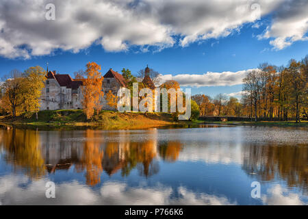 Un antico castello con torri su un isola dal lago tra Giallo autunno alberi con riflesso nell'acqua. Jaunpils Foto Stock