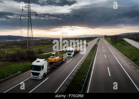 Trainare carrelli in un convoglio o caravan costruzione portante gli escavatori macchine lungo la statale Foto Stock