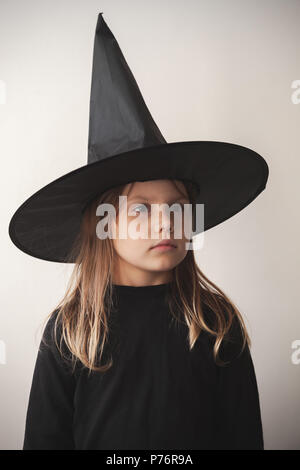 Grave poco bionda ragazza europea in black costume strega oltre il muro bianco, close-up ritratto in studio Foto Stock