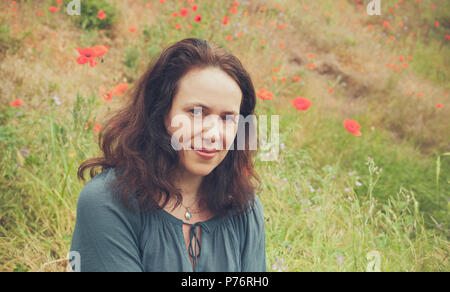 Sorridente giovane adulto donna europea su un prato estivo con la fioritura di papavero. Vintage nei toni del ritratto all'aperto Foto Stock