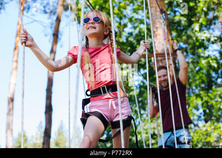 Ragazza vivace essendo seguita da padre a fune park Foto Stock