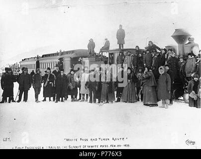 . Inglese: primo treno passeggeri del White Pass & Yukon Railroad sul vertice del Pass bianco, Alaska, 20 febbraio, 1899. Inglese: mostra la folla di uomini e donne, alcuni con telecamere, in piedi nella parte anteriore del treno. Didascalia sulla immagine: 'White Pass e Yukon Route". Primo treno passeggeri sul vertice del Pass bianco. Feb 20 1899." Immagine originale in Hegg Album 2, pagina 30. Soggetti (LCTGM): i binari della ferrovia--Alaska--Pass bianco; locomotive -- Alaska--Pass bianco soggetti (LCSH): White Pass & Yukon Route (Azienda) . 1899 5 primo treno passeggeri del Pass bianco &AMP; Yukon Railroad sul vertice del Foto Stock