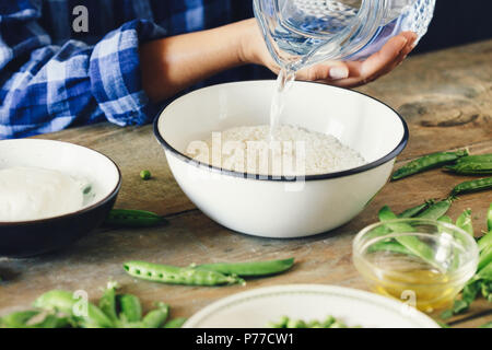 Cibo sano concetto. Donna vegetariana di cottura Risotto con piselli verdi, menta e formaggio di capra. Stile rustico. Materie prime per cucinare il risotto su woo Foto Stock