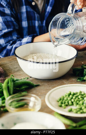 Cibo sano concetto. Materie prime per cucinare il risotto su un tavolo di legno. Donna vegetariana di cottura Risotto con piselli verdi, menta e formaggio di capra Foto Stock