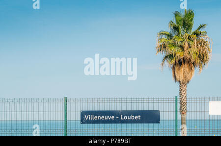 Segno di Villeneuve Loubet con un albero di palma e blu Mare Mediterraneo, Francia. Foto Stock