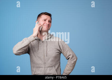 Irritato attraente uomo europeo nella ricezione di messaggio sgradevole o Chiamata di colore su sfondo blu. Foto Stock