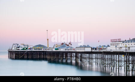 Il Brighton Pier (Molo Centrale) in Brighton, East Sussex, all alba con colorate sfumature pastello in un cielo privo di nuvole e liscia, calma acqua blu Foto Stock