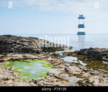 Penmon Lighthouse vicino a Beaumaris, Anglesey, su un luminoso, giornata soleggiata con rocce e alghe verdi rock pool in primo piano ed un cielo blu Foto Stock