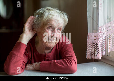 Un disco di udito donna anziana trattiene la sua mano vicino al suo orecchio. Foto Stock