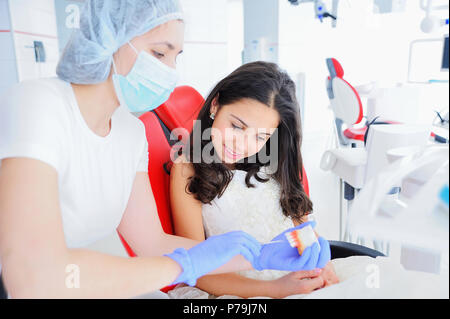 Ragazza giovane dentista in maschera mostra giovane bella ragazza dentiere. Foto Stock