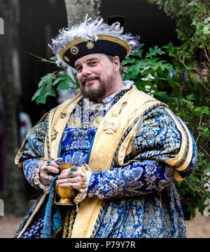 Maryland Renaissance festival attore raffigurante il re Enrico VIII in appoggio all'aperto, con un drink nel suo bejeweled mani. Egli è sempre sorridente rivolta verso la telecamera. Foto Stock