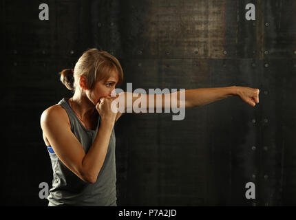 Close up side Visualizza profilo ritratto di una giovane età media athletic donna shadow boxing in abbigliamento sportivo in palestra su sfondo scuro, guardando lontano Foto Stock