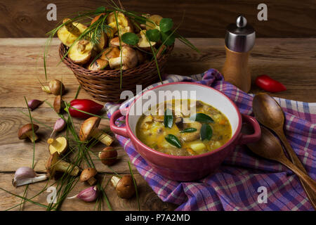 Zuppa di funghi in rosso coppa rustico e cesto di vimini con funghi sul tavolo di legno. Vegetariano cibo sano Foto Stock