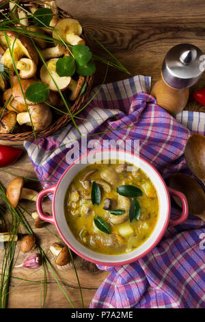 Funghi zuppa di verdure in rosso coppa rustico, cesto di vimini e pepe mulino sul tavolo di legno, vista dall'alto. Vegetariano cibo sano Foto Stock